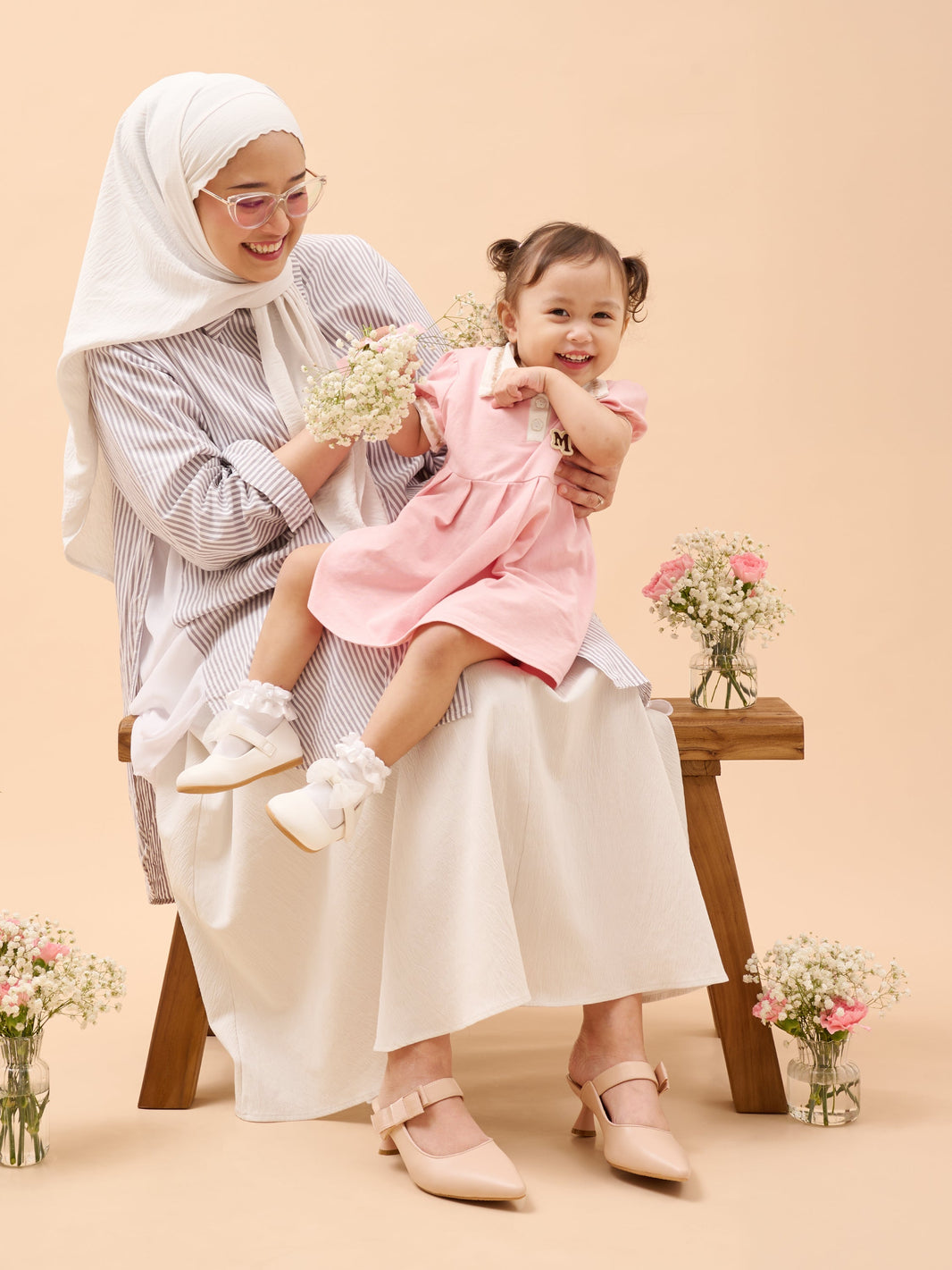 Atikah and her daughter wearing matching prettyFIT nude Mary Jane heels, sharing a joyful moment with flowers on a warm beige background.